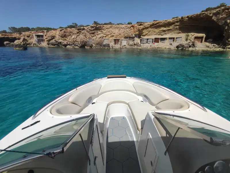 Solárium de proa de la Chaparral frente a las casetas de pescadores de una cala de Ibiza